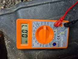 Pomarańczowy multimetr z wyświetlaczem pokazującym 0.00 i podłączonymi przewodami.