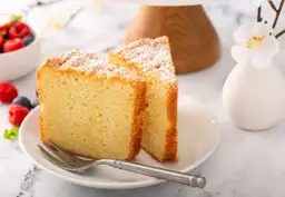 Dos porciones de pa de pessic, esponjoso y espolvoreado con azúcar glas, junto a frutos rojos y un tenedor.