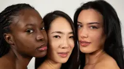 Tres mujeres de diferentes etnias, una con piel **color negro**, se miran a la cámara con labios brillantes.