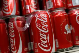 Puszki Coca-Coli ułożone na półce, jedna z nich z widoczną etykietą kaloryczną.