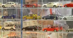 Modele samochodów w gablotach: białe kombi, czerwony sportowy, żółty hatchback, niebieski sedan, srebrny coupe.