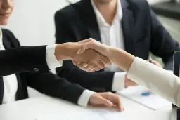 Dwie osoby w garniturach ściskają sobie dłonie, symbolizując udaną współpracę. To właśnie jest trade marketing co to znaczy - budowanie relacji biznesowych.