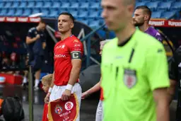 Piłkarz Wisły Kraków z kapitańską opaską, który awansował do ekstraklasy w piłce nożnej, trzyma flagę.