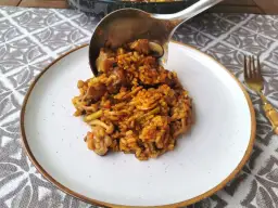 Un cucharón sirve arroz con secreto, un plato sabroso con carne y verduras, en un plato blanco.