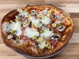 Pyszna pizza z twarogu z pieczarkami, szynką i oliwkami, zapieczona na złoto.