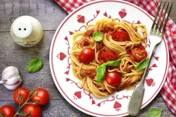 Makaron spaghetti z sosem pomidorowym, pomidorkami koktajlowymi i bazylią na talerzu.