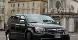 Czarny Lancia Voyager na tle zabytkowej architektury.