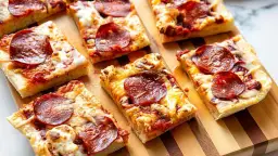 Kawałki pizzy pepperoni na desce. Dowiedz się, jak podgrzać pizzę na patelni, by była idealnie chrupiąca.