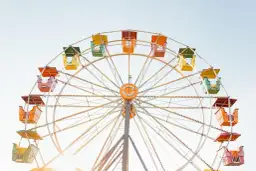 Grande roue colorée avec des nacelles jaunes, vertes, oranges et rouges sous un ciel clair.