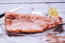 Surowy filet karpia na talerzu z cytryną i pieprzem, obok nóż.