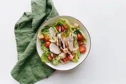 Sałatka cezar bez sosu worcestershire: grillowany kurczak, chrupiące grzanki, pomidorki koktajlowe i sałata rzymska polane kremowym dressingiem.