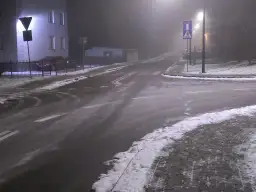 Skrzyżowanie dróg w nocy, z mgłą, śniegiem i znakami drogowymi.