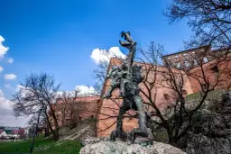 Smok Wawelski Kraków, groźny posąg smoka u stóp Wawelu, na tle ceglanych murów i błękitnego nieba.