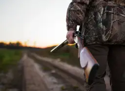 Myśliwy w kamuflażu trzyma strzelbę na drodze. Czy myśliwy może polować na prywatnym terenie?