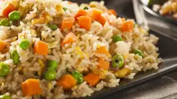 Arroz tres delicias con guisantes verdes, trozos de zanahoria y huevo revuelto, servido en un plato negro.