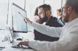 Analityk biznesowy wskazuje na wykres na monitorze, omawiając dane z kolegą.