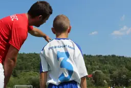Trener w czerwonej koszulce instruuje młodego piłkarza. Czy to jego pierwsza praca i zastanawia się, ile zarabia trener w okręgówce?