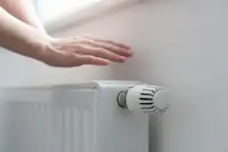 Dłoń nad grzejnikiem, sprawdzająca ciepło. Rozpoczyna się sezon grzewczy, czas na komfortowe ogrzewanie.