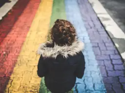 Dziecko z kręconymi włosami idzie po tęczowym przejściu dla pieszych.
