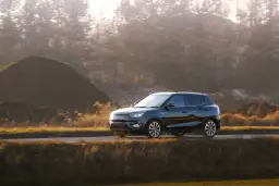 Czarny hatchback jedzie drogą wśród jesiennych wzgórz i drzew.