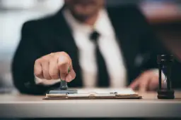 Biznesmen pieczętuje dokumenty, a klepsydra symbolizuje upływ czasu. To może być związane z tym, kompensata co to.