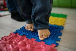 Dziecko w dżinsach staje na kolorowych, sensorycznych matach do ćwiczeń.