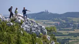 Trzech turystów na skale w Górach Świętokrzyskich, jeden wskazuje kierunek. W oddali widać ruiny zamku.
