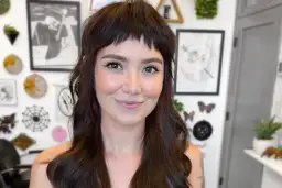 Uśmiechnięta kobieta z ciemnymi włosami i odważnymi baby bangs.