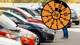 Rząd samochodów na parkingu z pomarańczową tarczą z numerami i cyfrą 25.