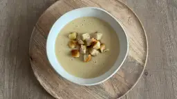 Aksamitna zupa cebulowa krem, udekorowana chrupiącymi grzankami, podana na drewnianej desce.
