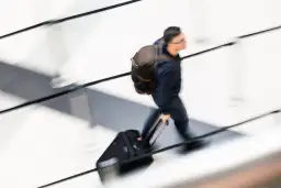 Mężczyzna z plecakiem i walizką na kółkach w ruchu.