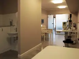 Gabinet okulistyczny z aparaturą medyczną, biurkiem i umywalką.