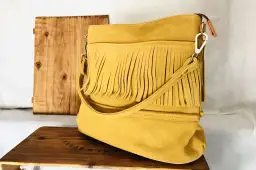 Bolso amarillo con flecos, de ante o serraje, sobre una caja de madera.