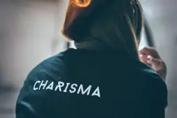 Osoba w bluzie z napisem "CHARISMA" na plecach, z włosami opadającymi na ramiona.