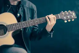 Dłoń gitarzysty na gryfie gitary akustycznej, grającego akord.