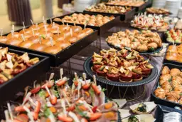 Stół z przekąskami: mini burgery, croissanty, tartinki, koreczki z owocami i mięsem.