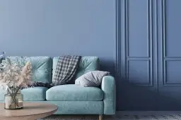 Miętowa kanapa z kocem i poduszką na tle ścian w kolorze baby blue. To znaczy spokój i świeżość.