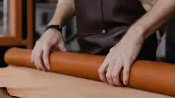 Manos de artesano desenrollando un rollo de cuero, mostrando la textura y el color natural del material. Se pregunta de que esta hecho el cuero.