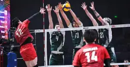 Zacięta akcja siatkarska: polska Japonia w akcji. Zawodnik w czerwonej koszulce atakuje, blokujący w zielonych strojach próbują zatrzymać piłkę.