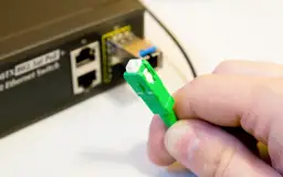Zielona wtyczka światłowodu gotowa do podłączenia do switcha w bloku. Szybki internet w zasięgu ręki.