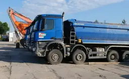 Niebieskie wywrotki i koparka stojące na placu budowy.
