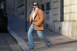 Mujer con abrigo camel, camisa blanca y jeans anchos, luciendo un bolso morado. Su estilo es muy aesthetic.