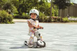 Uśmiechnięte dziecko w kasku na jeździku Scoot and Ride od kiedy zaczęło swoją przygodę z jazdą.