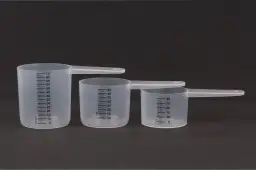 Trzy plastikowe miarki kuchenne z podziałką w mililitrach na ciemnym tle.