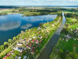 Malownicze pławniowice jezioro otoczone zielenią i domkami letniskowymi, z kanałem wodnym biegnącym równolegle.