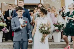 Para młoda trzymająca się za ręce, otoczona bańkami mydlanymi i gośćmi weselnymi.