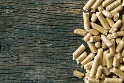 Drewniane deski i stos pelletu. Czy pellet jest ekologiczny? To pytanie zadaje sobie wielu, a ten obrazek pokazuje jego naturalne pochodzenie.