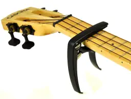 Czarny kapodaster do ukulele marki Moge na drewnianej podstrunnicy z widocznymi progami i strunami.