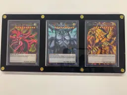 Trzy karty Yu-Gi-Oh! w ramce: Slifer the Sky Dragon, Obelisk the Tormentor i The Winged Dragon of Ra.