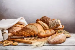 Różnorodne pieczywo, od bochenków po bułki, ułożone na desce. Idealne do odświeżenia bułki na śniadanie.